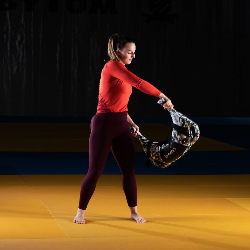 Sportoló nő funkcionális edzést végez HMS bolgárzsákkal, teljes testet megdolgoztató gyakorlat közben